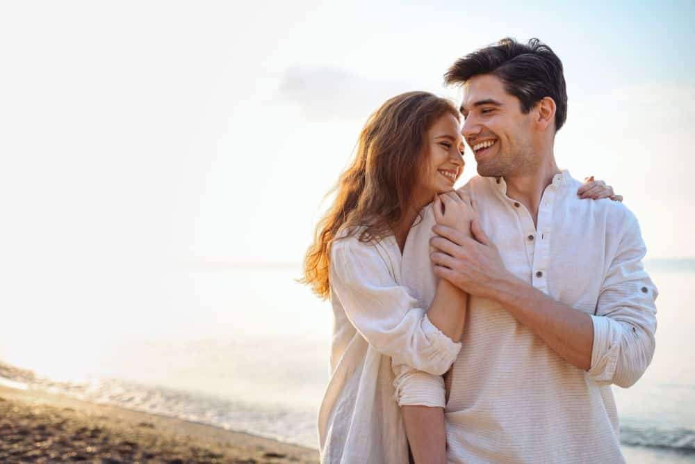 happy cuddling couple walking on a beach by sunset