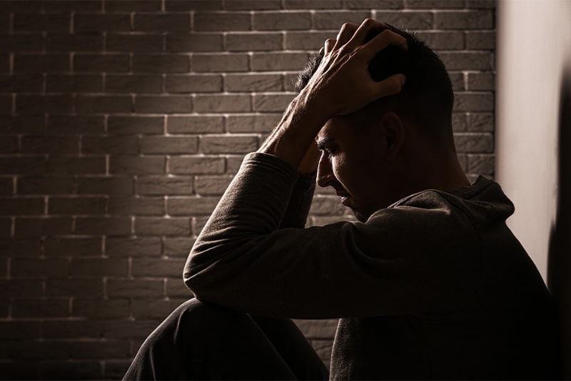 A man sits against a brick wall in a dimly lit room