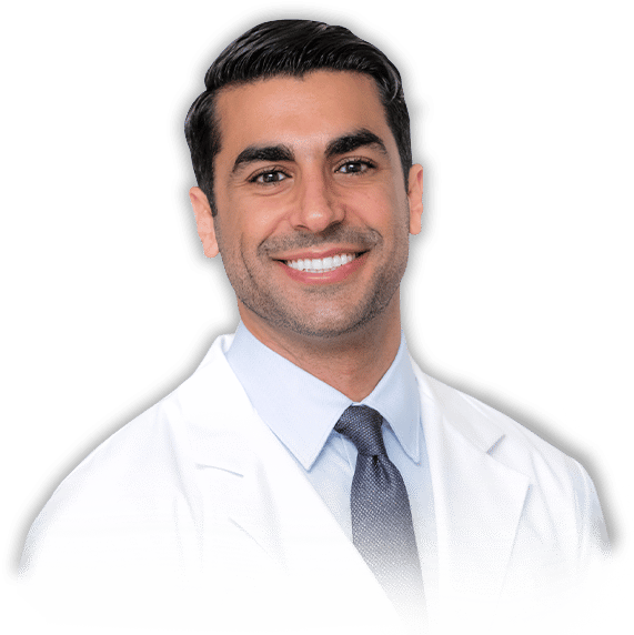 Smiling man with dark hair wearing a white lab coat, light blue shirt, and gray tie, posing against a plain light background.