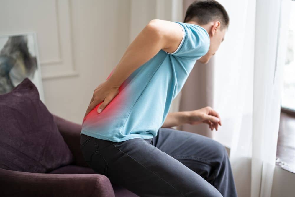 A man trying to get up from the armchair feeling sharp pain in the lower back due to kidney stones