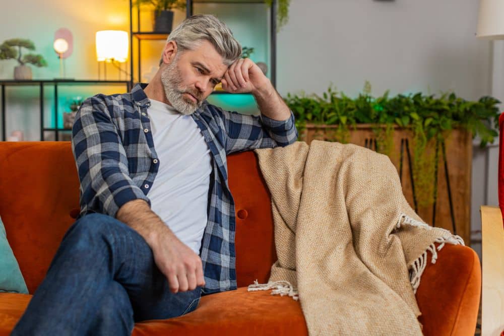 A middle-aged man with gray hair and a beard sits on an orange sofa
