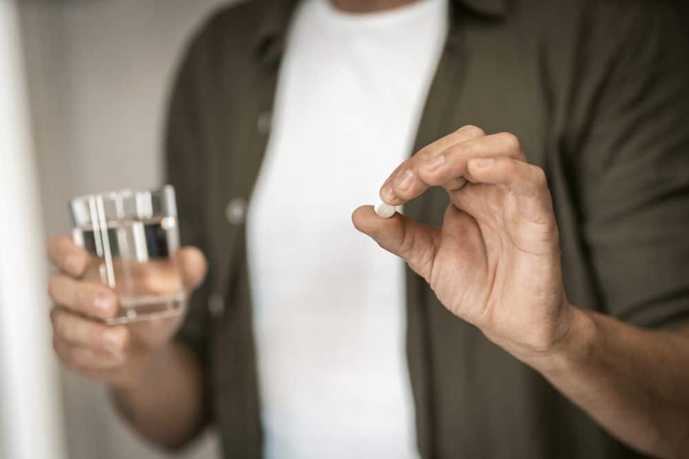 A man holding a pill in one hand and a glass of water in the other one.