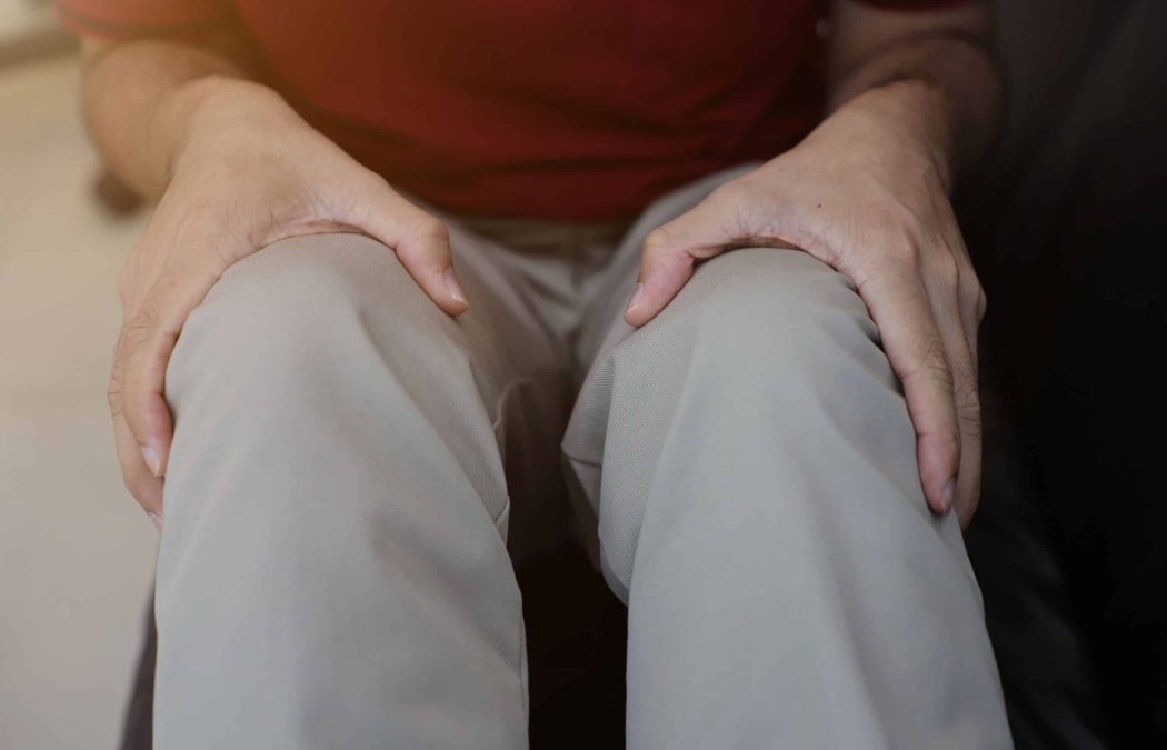 A person wearing beige pants sits with hands resting on their knees.