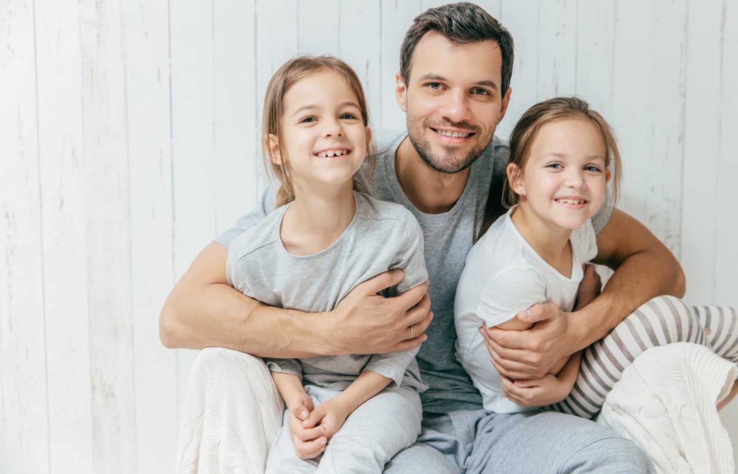 Portrait of happy young father embraces his two daughters