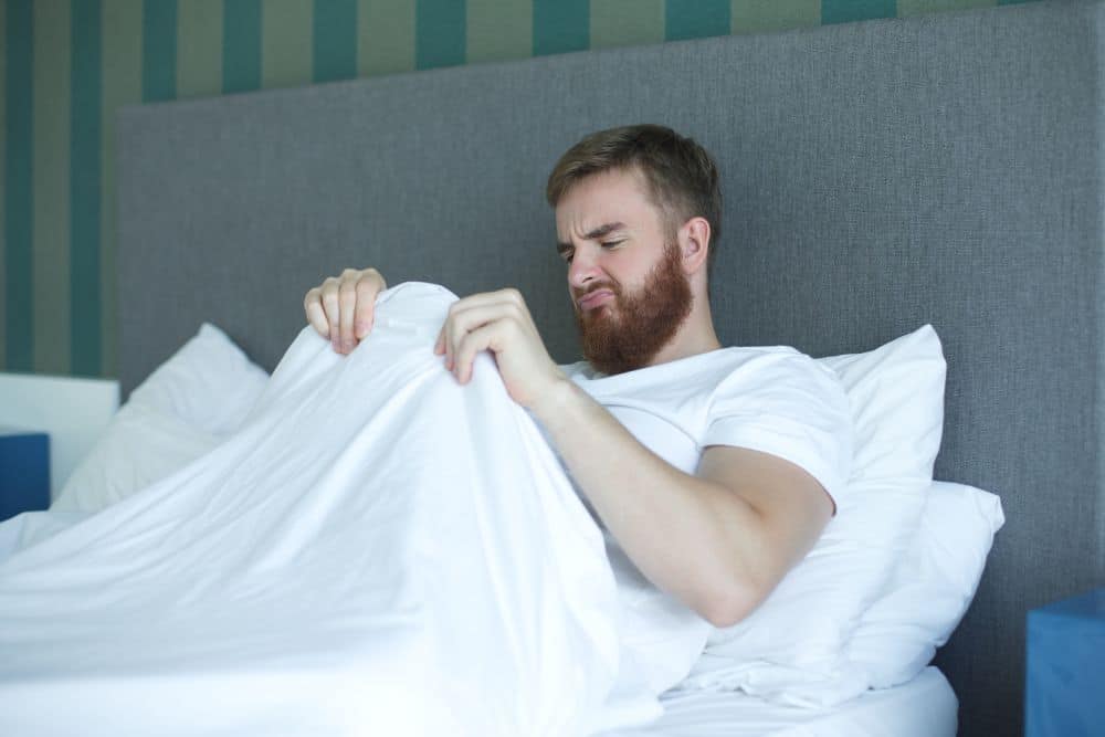 A worried man disappointed with missing morning erection looking under duvet after waking up