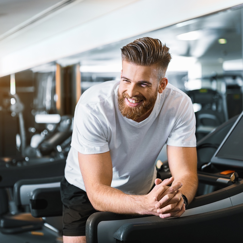 Hilarious sporty guy is standing at treadmill. He having some rest