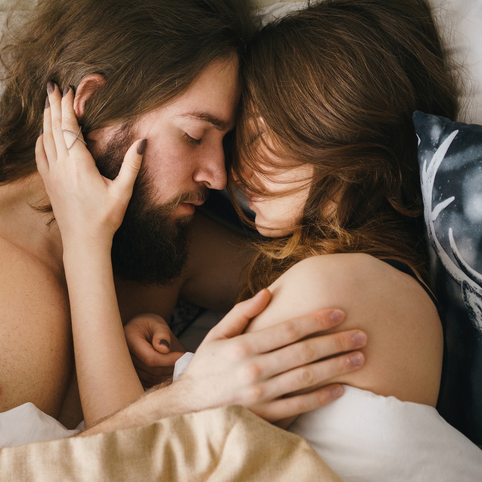 From above shot of young naked couple embracing in bed with eyes closed.