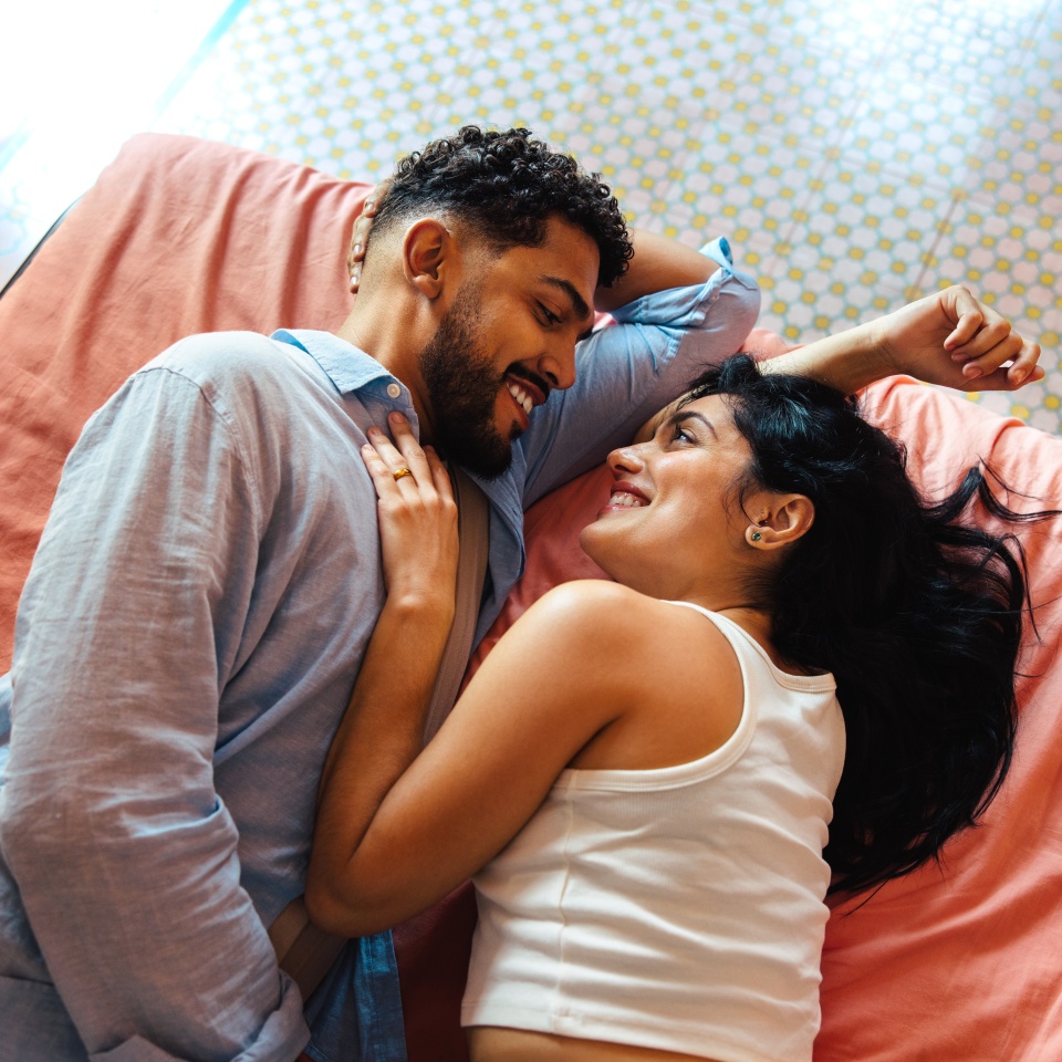 A happy couple enjoying a close and intimate moment, lying together on a bed indoors, portraying love and affection.
