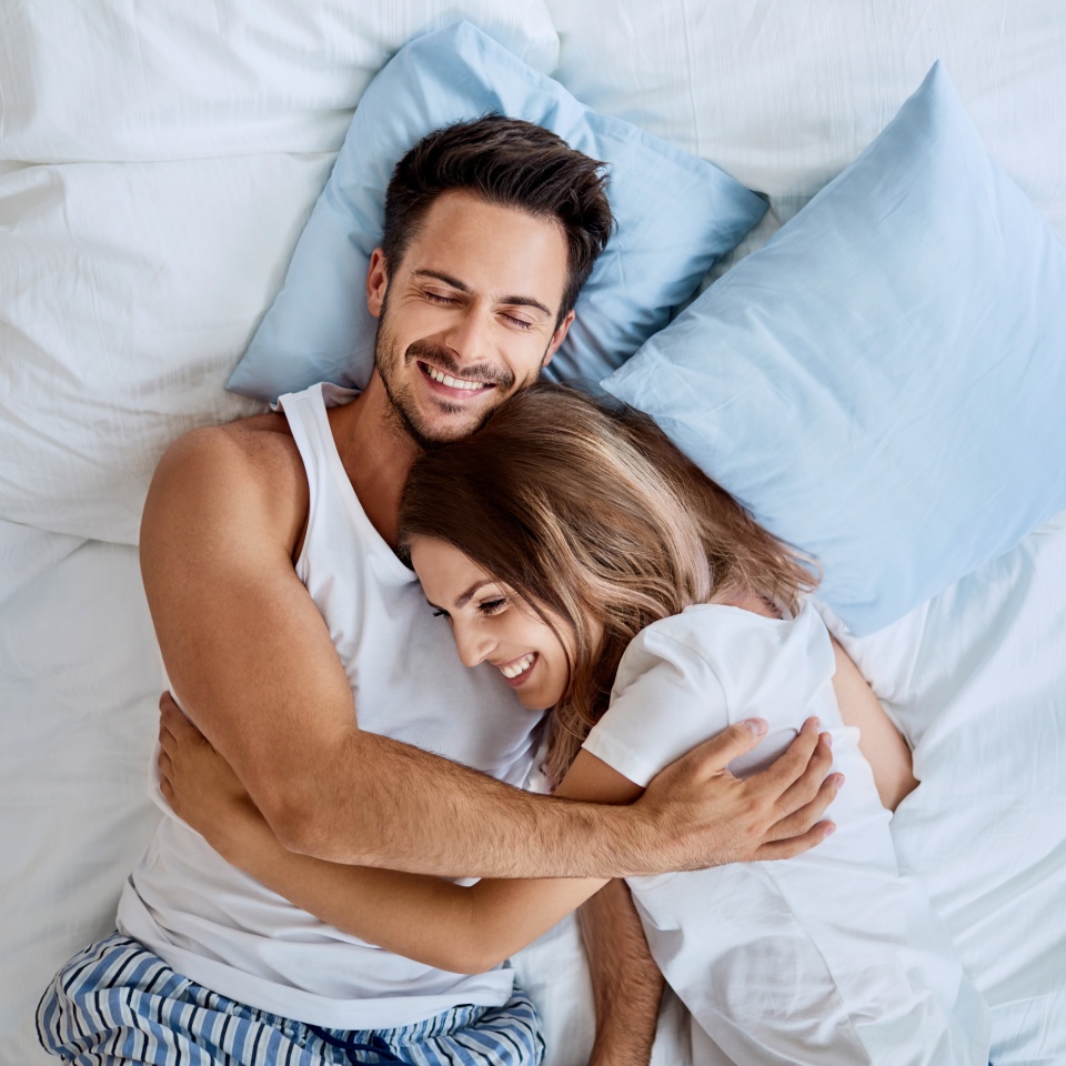 Top view of beautiful happy young couple lying on bed and hugging