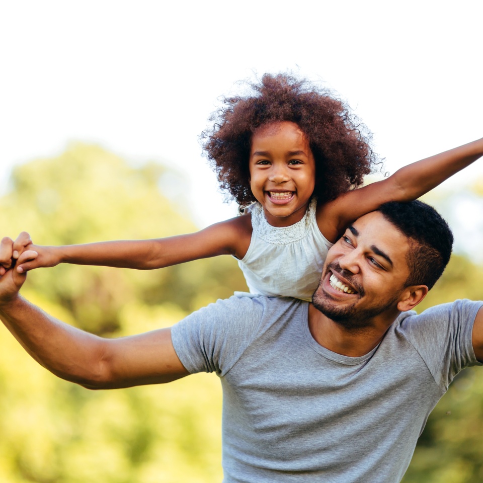 Portrait of young father carrying his daughter on his back in nature
