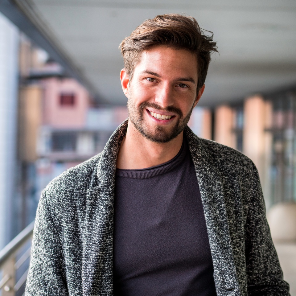 One handsome young man in urban setting in European city, standing and smiling to camera happy