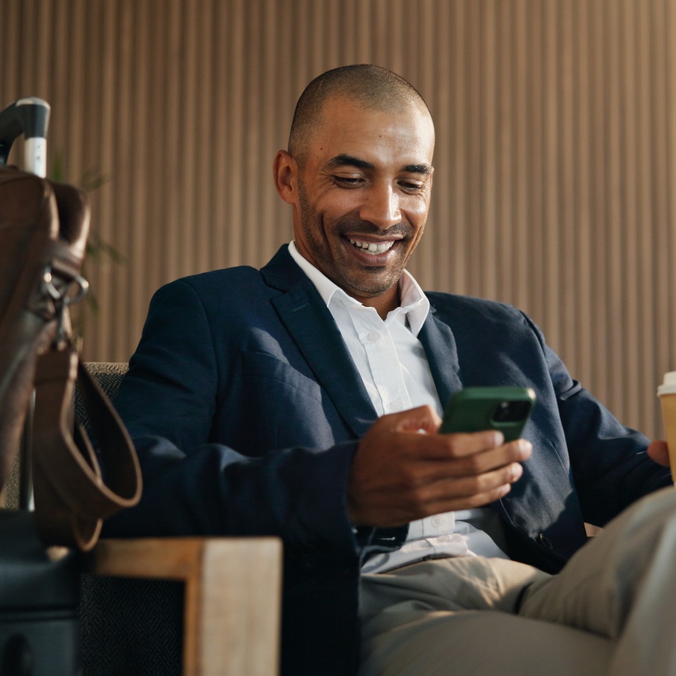 Trader, smile and man in airport, smartphone for online flight schedule and coffee with chatting. Happy person, latte and investor on chair, cellphone and email for visa application and trading info.
