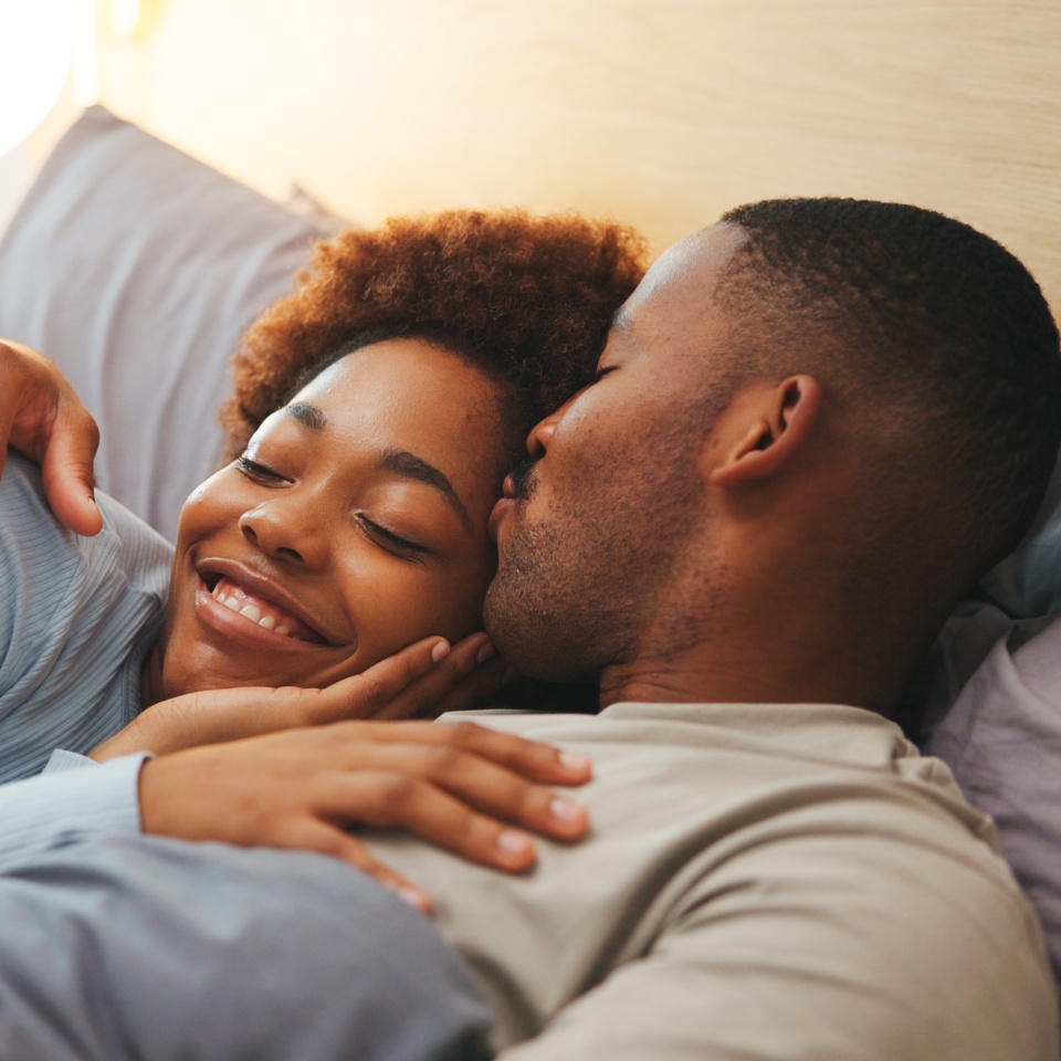 Kiss, love and relax with black couple in bed at apartment together for bonding, connection or rest. Affection, morning and wake up with happy people in bedroom of home for break, holiday or romance.