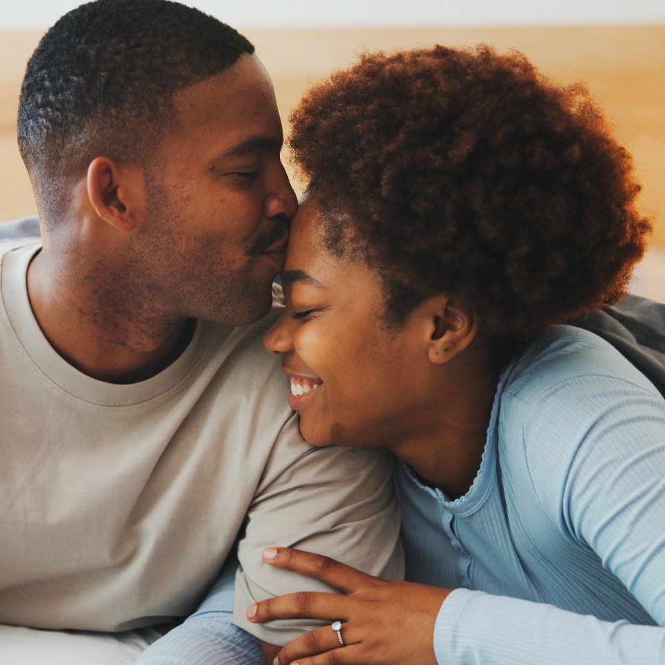 Forehead, kiss and smile with black couple in bed at apartment together for bonding, connection or rest. Affection, love and wake up with happy people in bedroom of home for break, holiday or romance.