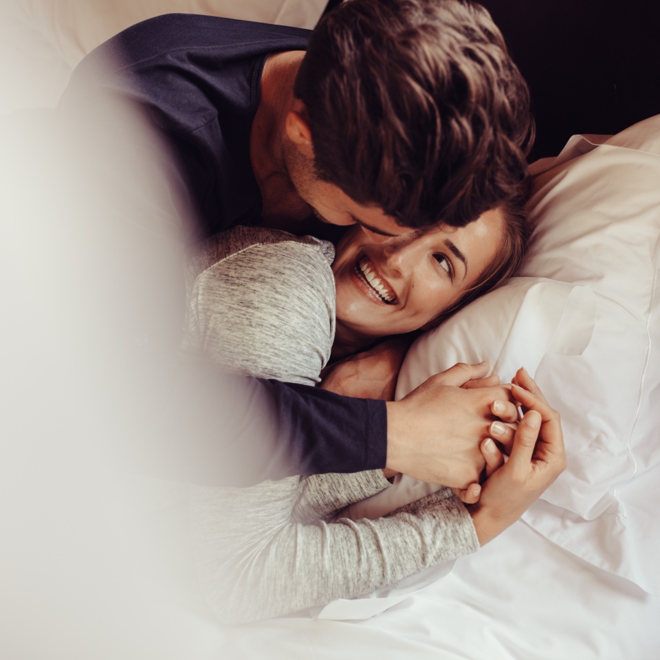 Romantic young couple in love lying on bed. Beautiful couple smiling in bed.