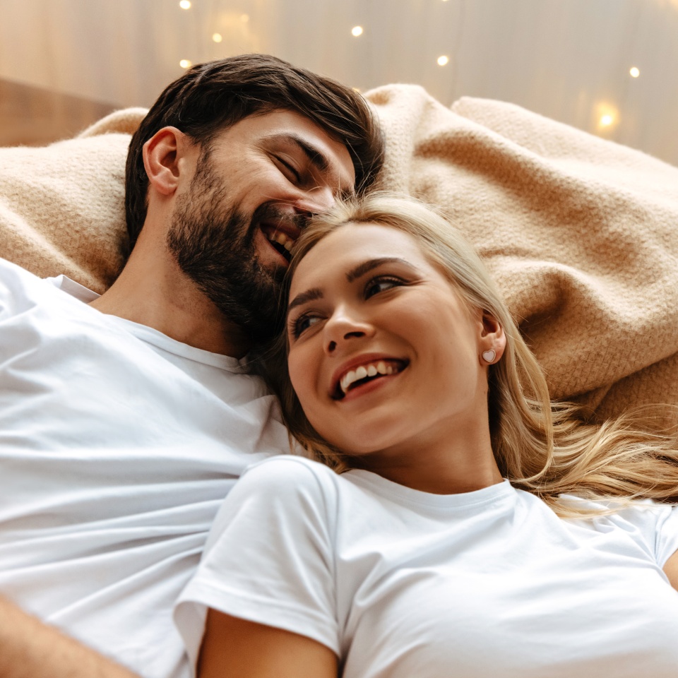 Love. Fun. Emotions. Young couple are laughing while lying together on the bed