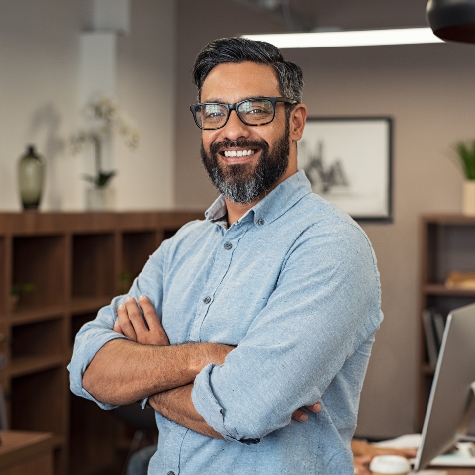Portrait of happy mature businessman wearing spectacles and looking at camera. Multiethnic satisfied man with beard and eyeglasses feeling confident at office. Successful middle eastern business man smiling in a creative office.