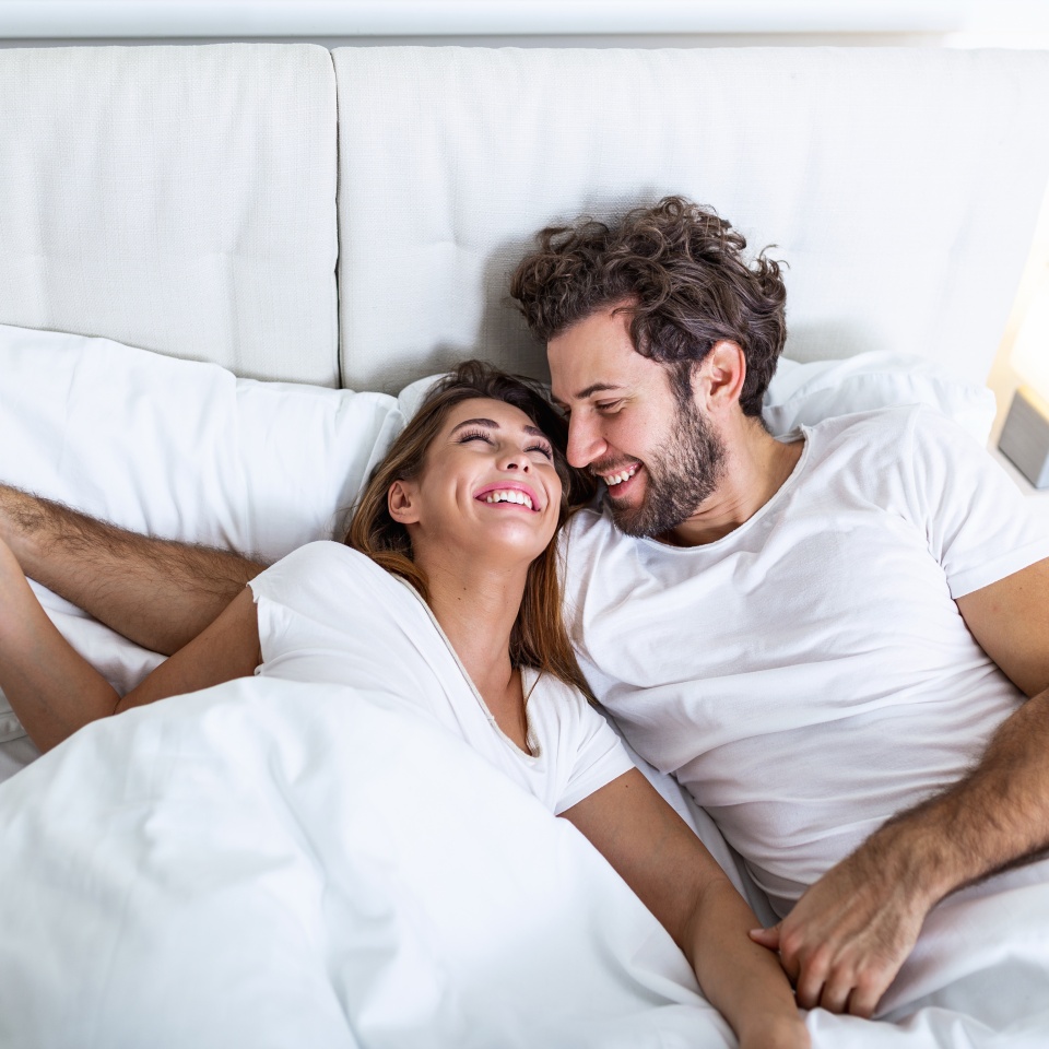 Young loving couple in the bed. Young couple lying in bed and laughing while tickling each other. Happy sensual young couple lying in bed together in the morning