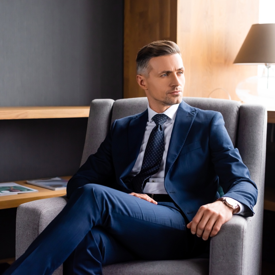 handsome businessman in suit sitting in armchair and looking away
