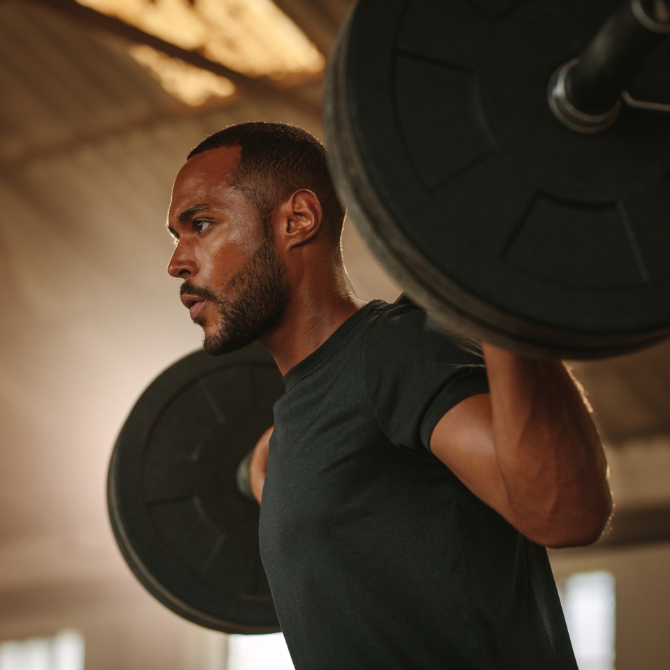 Man exercising with barbell. Male bodybuilder doing weight lifting workout at cross training gym.
