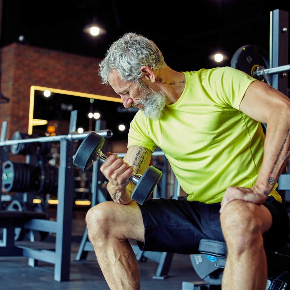 Gaining muscles after 40. Strong mature man in sportswear lifting heavy dumbbells and pumping his biceps while working out at gym. Training, sport, bodybuilding concept