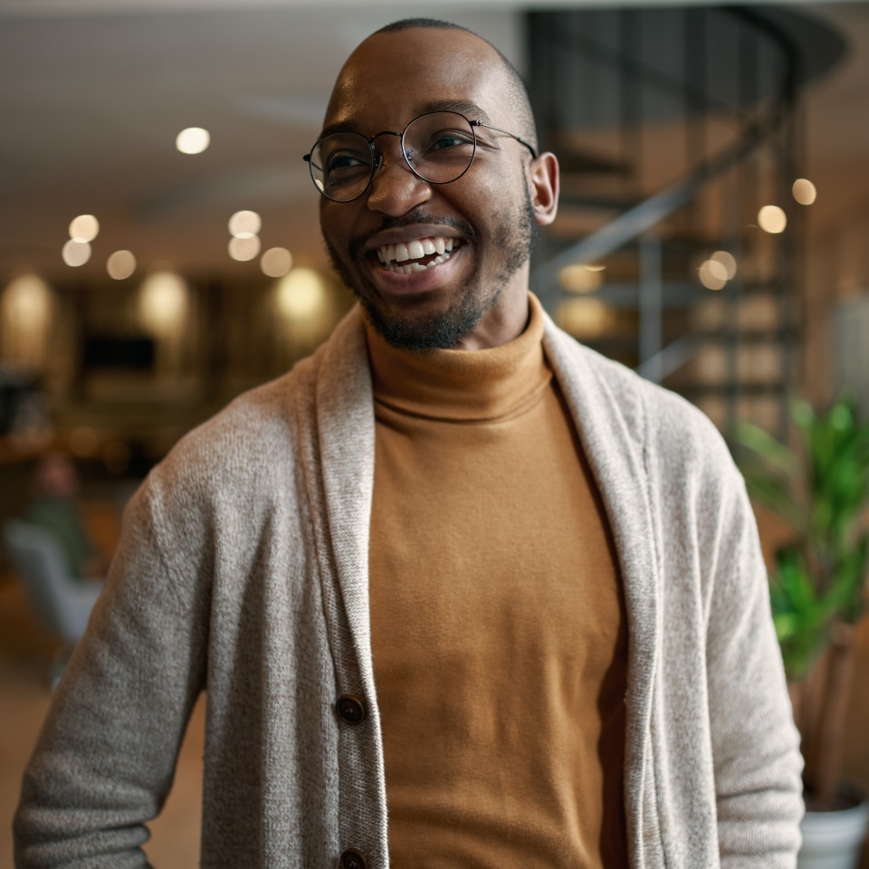 Happy portrait of african entrepreneur laughing and smiling. feeling excited and positive. Wearing trendy clothing and eye glasses in a modern working space