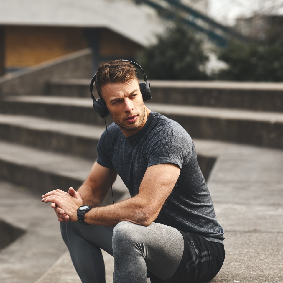 Attractive sport man listening to music via smartphone and headphones in urban environment