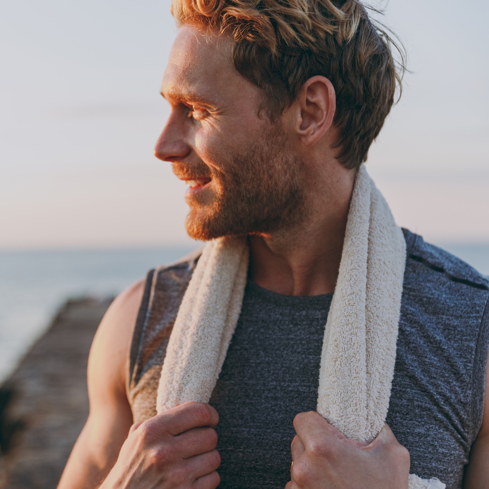 Close up happy young strong sporty athletic toned fit sportsman man in sports clothes towel warm up train look aside at sunrise sun dawn over sea beach outdoor on pier seaside in summer day morning.