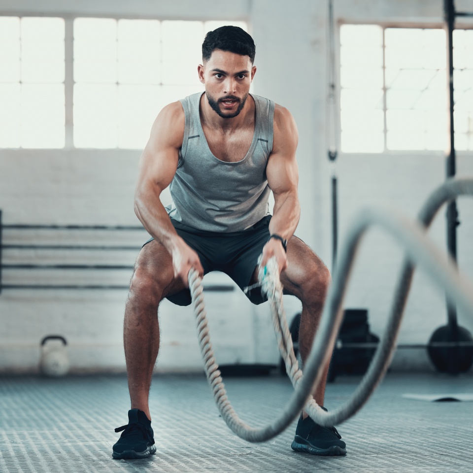 Shot of a young man using the ropes in the gym to build arm strength.