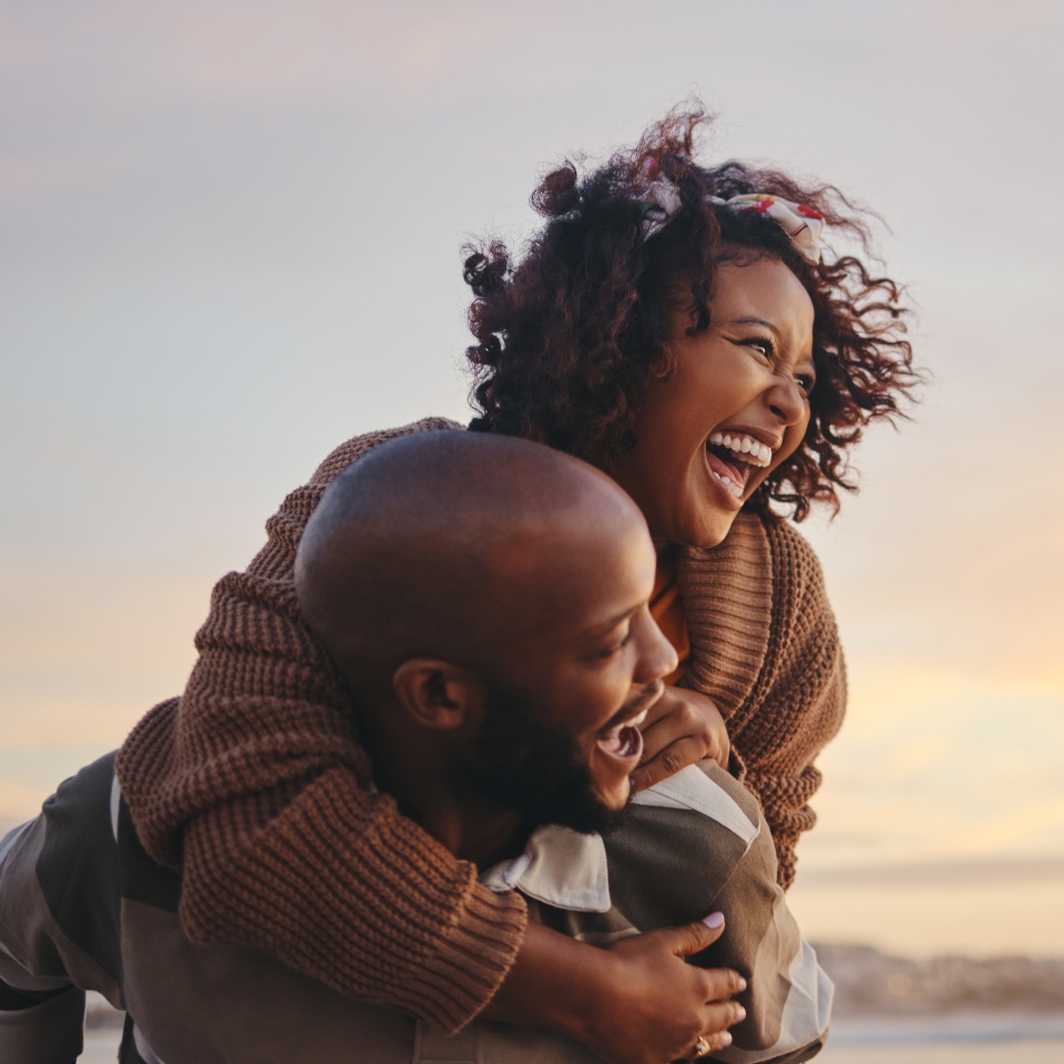 Black couple, travel and beach fun while laughing on sunset nature adventure and summer vacation or honeymoon with a piggy back ride. Comic, energy and black man and woman love on ocean holiday.