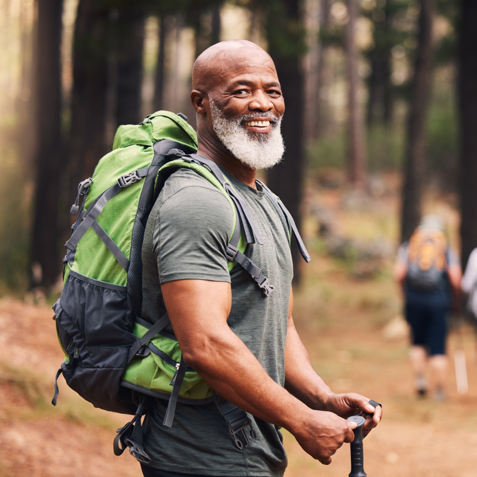 Portrait, black man and hiking in forest, exercise and fitness for wellness, healthy lifestyle and smile. Face, senior male and mature gentleman with backpack, smile and hiker in woods and fresh air.