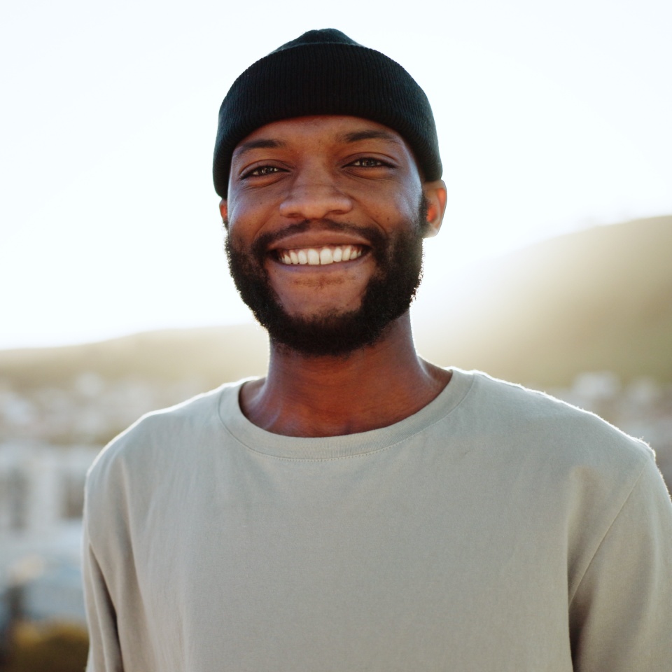 Face, happy and street style with a black man outdoor in the city with nature in the background during summer. Portrait, fashion and urban with a handsome young male standing outside in a bright town.