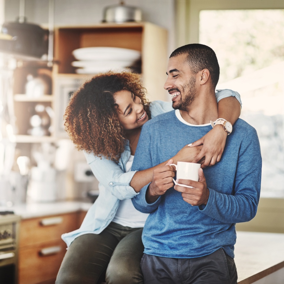 Love, coffee and happy couple in kitchen, morning hug in home with smile, hugging and healthy relationship. Happiness, man and woman embrace with affection, romance and young people in apartment
