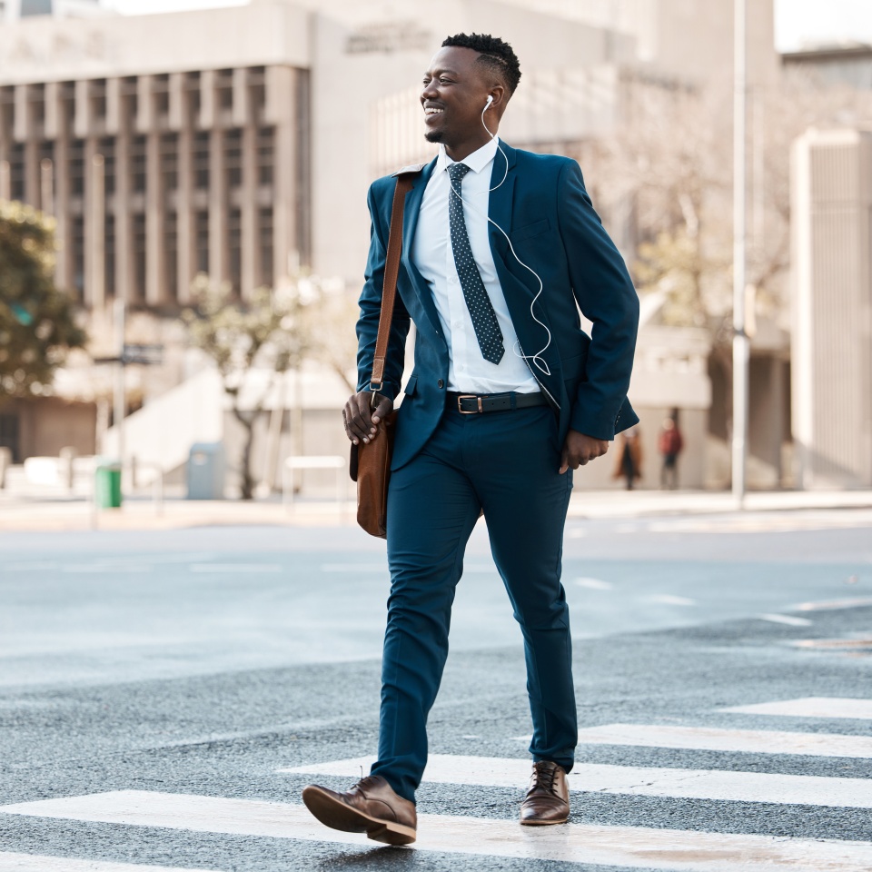 Happy businessman, walking and city to work for travel on street or pedestrian crossing outdoors. Black man on cross road, walk or traveling to business with suit and smile on asphalt in urban town.