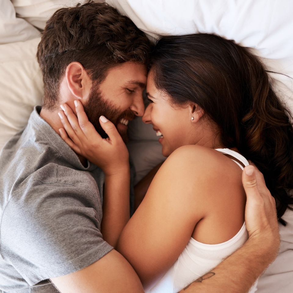 Smile, bed and happy couple hug, relax and spending lazy morning together, bonding and intimacy on Spain vacation. Happiness, marriage and top view of romantic man, woman or people embrace in bedroom.
