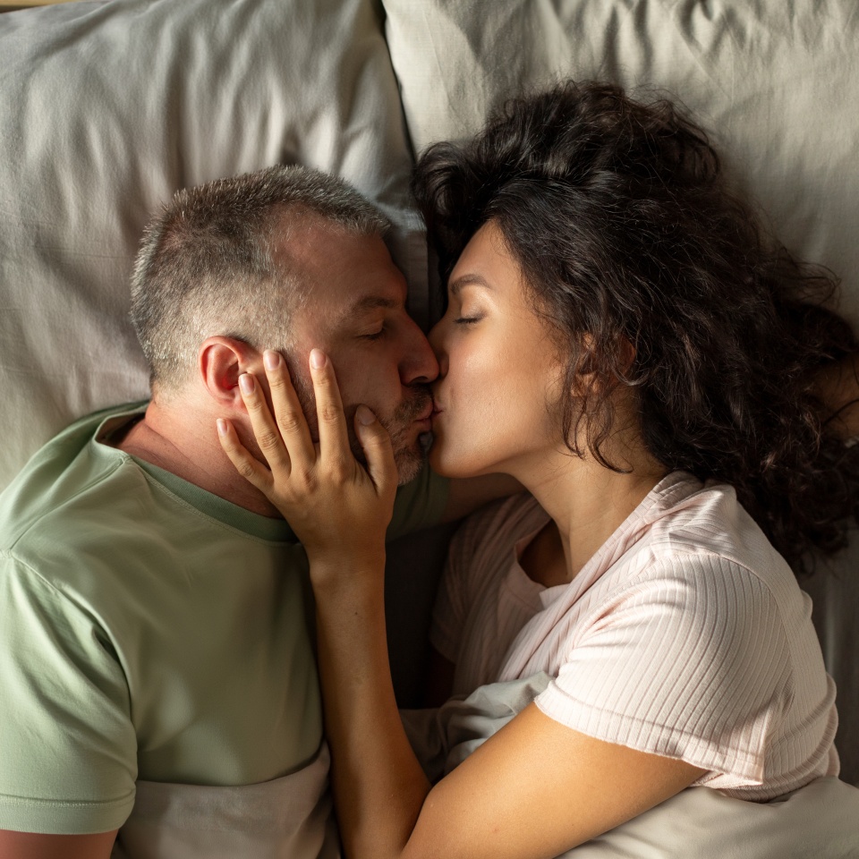 Spouses kissing, lying on the bed at the morning, top view shot. Love, happiness, family concept