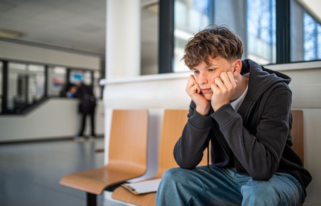 Anxious teenager waiting alone in hospital waiting area before medical checkup.